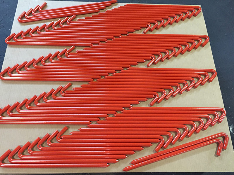 a plethora of red enameled hook style tent stakes is layed out on a piece of cardboard