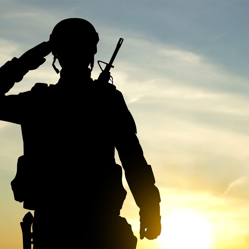 Silhoette of US marine saluting in combat gear at field camp